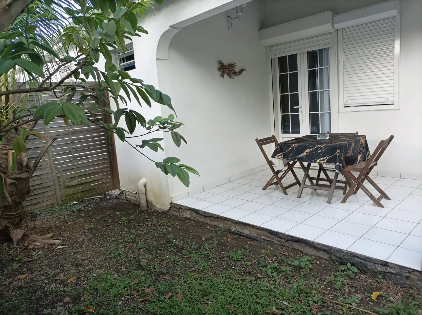 Terrasse carrelée avec table et chaises pliantes, devant les portes-fenêtres du studio